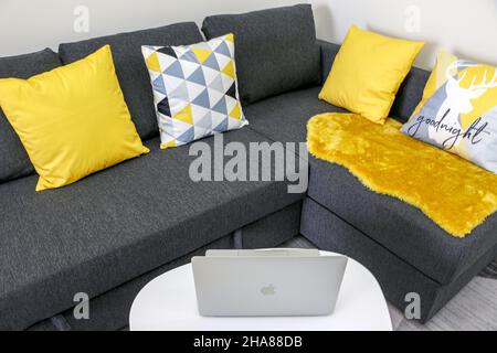 Öffnen Sie Macbook Pro auf einem Tablet vor dem Grey Sofa mit gelben und gemusterten Kissen Stockfoto