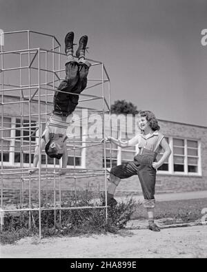 1950S JUNGE UND MÄDCHEN SPIELEN AUF SPIELPLATZ DSCHUNGEL FITNESS-STUDIO JUNGE ZEIGEN, HÄNGEN KOPFÜBER VON DER BARS MÄDCHEN STEHEN BY LACHING - J5068 HAR001 HARS OLD FASHION SISTER 1 JUVENILE FRIEND BALANCE SAFETY COMPETITION BAUMWOLLE FREUDE LIFESTYLE DSCHUNGEL WEIBCHEN BRÜDER ZEIGEN LÄNDLICHE GESUNDHEIT KOPIEREN RAUM FREUNDSCHAFT GANZKÖRPERLICHKEIT PERSONEN MÄNNER RISKIEREN AUFWÄRTSPOTENZIAL GESCHWISTER VERTRAUEN DENIM SCHWESTERN B&W BARS SUMMERTIME HAPPINESS WELLNESS ABENTEUER FREIZEIT STRATEGIE UND AUFREGUNG ERHOLUNG STOLZ DURCH DIE MÖGLICHKEIT DER GESCHWISTER KONZEPTIONELL FREUNDLICH STILVOLLE BLAUE JEANS WACHSTUM INFORMELLE JUGENDLICHE PRE-TEEN Stockfoto