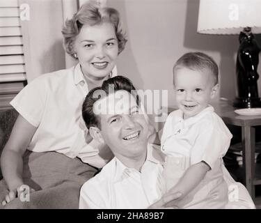 1950S PORTRÄT DER LÄCHELNDEN FAMILIE VON DREI MUTTER VATER KLEINKIND JUNGEN BLICK AUF DIE KAMERA IM WOHNZIMMER SITZEN - J5390 HAR001 HARS BEAUTY SUBURBAN MOTHERS OLD TIME FUTURE NOSTALGIA OLD FASHION 1 JUVENILE YOUNG ADULT BALANCE TEAMWORK SONS FREUTE FAMILIEN FREUDE LIFESTYLE ZUFRIEDENHEIT FEIER FRAUEN VERHEIRATET EHEGATTEN EHEMÄNNER GESUNDHEIT HEIM LEBEN KOPIEREN RAUM HALBE LÄNGE DAMEN PERSONEN INSPIRATION FÜRSORGLICHE MÄNNER VERTRAUEN VÄTER B&W PARTNER BLICKKONTAKT ERFOLG TRÄUME GLÜCK WELLNESS FRÖHLICH KRAFT WOHNZIMMER VÄTER STOLZ AUTORITÄT LÄCHELT VERBINDUNG FREUDIG STILVOLLES WACHSTUM DER MITTELSCHICHT Stockfoto