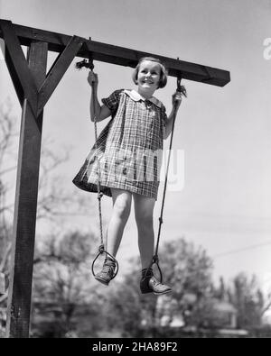 1930S LÄCHELNDES MÄDCHEN IN EINEM KARIERTEN KLEID AUF EINEM SPIELPLATZGERÄT, DAS MIT JEDEM FUSS IN EINEM PAAR STEHT GYMNASTIK O RINGE - J593 HAR001 HARS WETTKAMPF ATHLET FREUDE LIFESTYLE FRAUEN LÄNDLICHE GESUNDHEIT RINGE HEIMLEBEN LEICHTATHLETIK IN VOLLER LÄNGE KÖRPERLICHE FITNESS GEFAHR RISIKO SPORTLICH KARIERT S/W ZIELE ERFOLG AKTIVITÄT GLÜCK KÖRPERLICHES WOHLBEFINDEN FRÖHLICHES ABENTEUER FREIZEIT KRAFT MUT WAHL AUFREGUNG FÜHRUNG NIEDRIG WINKEL O ERHOLUNG STOLZ LÄCHELT SCHWINGENDE TOMBOY KONZEPTIONELLE ATHLETEN FLEXIBILITÄT GYMNASTIK FREUDIGE MUSKELN WACHSTUM JUVENILES APPARAT SCHWARZ UND WEISS, MUTIG Stockfoto