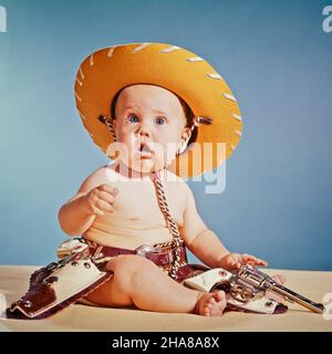 1960S BABY JUNGE MIT ÜBERRASCHTER GESICHTSAUSDRUCK ALS COWBOY GEKLEIDET TRÄGT HUT UND HOLSTER UND WAFFE - KB6910 HAR001 HARS BLICKKONTAKT COWBOYS ABENTEUER AUFREGUNG BRÖTCHEN UNTERSTÜTZUNG HOLSTER BABY JUNGE SCHUSSWAFFE SCHUSSWAFFEN JUGENDLICHE KAUKASISCHE ETHNIE HAR001 ALTMODISCH Stockfoto