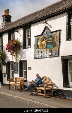 Großbritannien, Cumbria, Allerdale, Keswick, Threlkeld, Mann liest in Sonnenschein unter Jennings Brewery Horse und Farrier Pub Schild Stockfoto