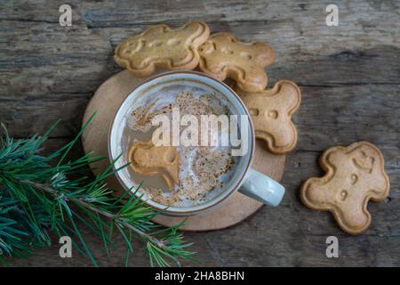 noel-Kekse, Cappuccino oder Latte-Kaffee und Lebkuchenkekse auf einem Holztisch, der mit Kiefernzweigen zu Weihnachten oder Neujahr geschmückt ist. Mann Stockfoto