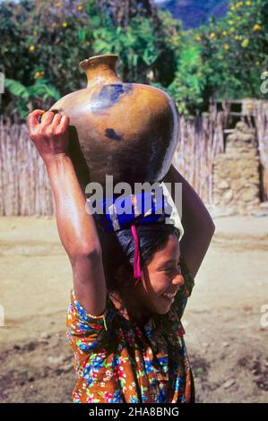 1970S ÖRTLICHE GUATEMALTEKERIN, DIE EINEN GROSSEN TONWASSERKRUG AUF DEM KOPF TRÄGT SAN ANTONIO GUATAMALA - KR26258 SPE001 HARS HALBLANGE DAMEN PERSONEN ANTONIO KERAMIK FRÖHLICHE ARBEIT TON NIEDRIG ANGESETZT LOKALE LÄCHELT AUFGABEN FREUDIGER KRUG GUATEMALA AUFGABE JUNGE ERWACHSENE FRAU MITTELAMERIKA ZENTRALAMERIKANISCHE HISPANISCHE ETHNIE ALTMODISCH Stockfoto