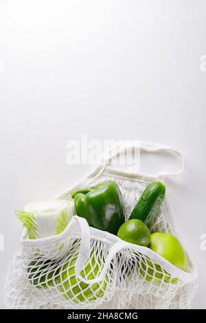 Grünes Obst und Gemüse im weißen Saitenbeutel. Grüne Äpfel, Limette, Gurke, Paprika und Kohl in einem wiederverwendbaren Baumwollbeutel auf weißem Bac Stockfoto