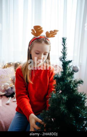 Mädchen in einem weihnachtskostüm schmückt den weihnachtsbaum Stockfoto