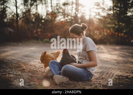 Mädchen, das auf der unbefestigten Auffahrt mit Hühnern sitzt Stockfoto