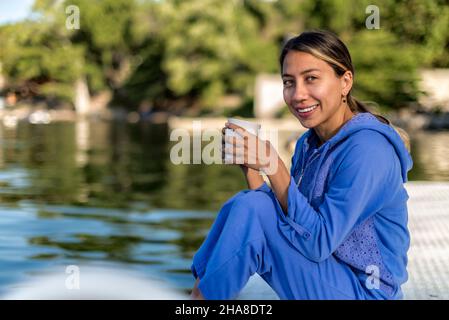 Lateinisches Mädchen mit Kaffee an einem See in einem Sommermorgen lächelnd Stockfoto