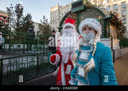 Moskau, Russland. 11th. Dezember 2021 Pater Frost (russisch: DED Moroz) und Snegurochka in Gesichtsmaske begrüßen die Gäste auf der Messe der Reise zum Weihnachtswinterfest auf dem Tverskaya-Platz im Zentrum von Moskau, Russland Stockfoto