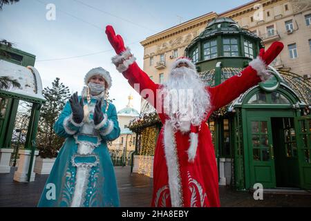 Moskau, Russland. 11th. Dezember 2021 Pater Frost (russisch: DED Moroz) und Snegurochka in Gesichtsmaske begrüßen die Gäste auf der Messe der Reise zum Weihnachtswinterfest auf dem Tverskaya-Platz im Zentrum von Moskau, Russland Stockfoto