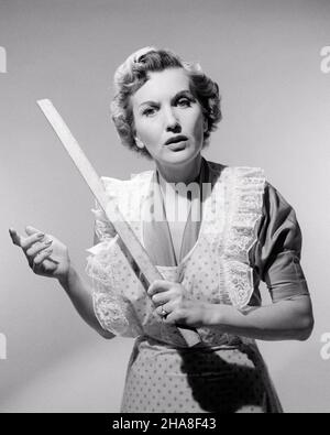 1950S 1960S SERIÖSE HAUSFRAU MUTTER TRÄGT SCHÜRZE BLICK AUF KAMERA HALTEN YARD STICK BETONT EINEN PUNKT DER ORDNUNG ODER DISZIPLIN - S4338 CLE003 HARS HALBLANGE DAMEN PERSONEN DISZIPLIN BEUNRUHIGT B&W BESORGT TRAURIGKEIT BLICKKONTAKT HAUSFRAU HAUSFRAU STRATEGIE HERRSCHER MÄCHTIG EIN AUTORITÄT HAUSFRAUEN STIMMUNG KONZEPTUELLE GLUM ODER MID-ADULT MID-ADULT FRAU MISERABLE LÖSUNGEN BETONEN YARD STICK SCHWARZ UND WEISS KAUKASISCHEN ETHNIE ALT MODISCH Stockfoto