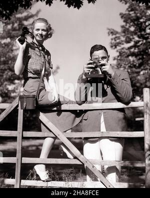 1930S PAAR BEIM LANGLAUFSPORT MANN FOTOGRAFIERT MIT KAMERA FRAU HÄLT FERNGLAS AM ZAUN - U343 HAR001 HARS WOHLHABEND ENTSPANNEND REICHEN LEBENSSTIL FRAUEN VERHEIRATET VERANSTALTUNG LÄNDLICHEN EHEGATTEN EHEMÄNNER KOPIEREN RAUM FREUNDSCHAFT HALBLÄNGE DAMEN PERSONEN MÄNNER ZUSCHAUER B&W PARTNER BLICKKONTAKT DATING GESCHICKLICHKEIT AKTIVITÄT UNTERHALTUNG SPORT ABENTEUER HOBBY BEOBACHTER INTERESSE UND AUFREGUNG HOBBYS WISSEN ZEITVERTREIB VERGNÜGEN ATTRAKTION GEHOBENER BEOBACHTER BALZ WOHLHABEND BEOBACHTEN STILVOLLE BETRACHTER MÖGLICHKEIT CROSS-COUNTRY MID-ADULT MANN MITTLEREN ERWACHSENEN ENTSPANNUNG SOZIALE AKTIVITÄT ZWEISAMKEIT Stockfoto