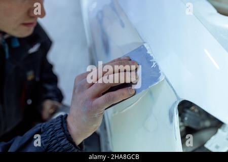 Reparatur der Karosserie durch Verputzen von Naharbeiten nach dem Unfall durch Arbeiten mit Schleifgrundierung vor dem Lackieren. , der Mechaniker reparieren das Auto , mit Stockfoto