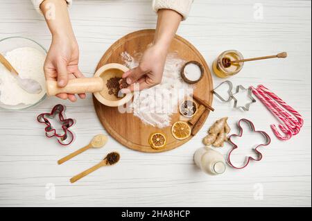 Man kann aus der Perspektive sehen, wie die Hände der Frau Gewürze in einen Marmormörtel gießen, während sie auf dem Küchentisch Weihnachtskekse zubereiten. Flach liegend Stockfoto