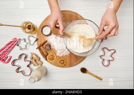 Flach liegend. Frauenhände mischen trockene Zutaten in einer Schüssel mit Mehl, während sie Lebkuchenteig für Weihnachtsplätzchen zubereiten. Essen, Kulinarik, Feiern Stockfoto