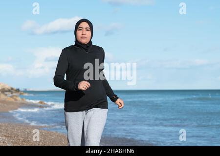 Arabische Frau, die am Strand am Meer läuft Stockfoto