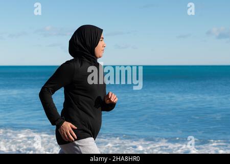 Arabische Frau, die am Strand mit dem Meer und dem Horizont im Hintergrund läuft Stockfoto