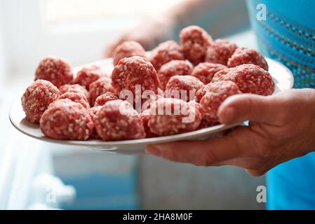 Weibliche Hände halten einen Teller mit viel Frikadelle - flache, gebratene Fleischbällchen aus Hackfleisch Stockfoto