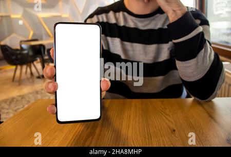 Die Hand des Mannes hält das Smartphone, das Bild der Hand zeigt das Mobiltelefon mit einem weißen Bildschirm. Stockfoto