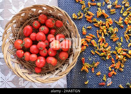 Tomaten und Paprika, frische Tomaten im Korb mit Weidenkorb und getrocknete Paprika auf blauem Deckel. Essenskonzept und -Idee. Stockfoto