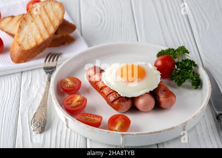 Spiegeleier mit Würstchen, Tomaten und Toast auf weißem Holzhintergrund Stockfoto