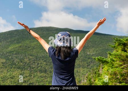Eine Frau, die triumphierend mit ausgebreiteten Armen das Mount Field von der Spitze des Mount Willard in Crawford Notch in den weißen Bergen von New hampshire aus betrachtet. Stockfoto