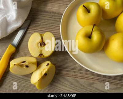 Gelbe Äpfel, goldgelbe Äpfel auf einem weißen Teller. Messer mit geschnittenen Scheiben auf einem Holztisch. Lebensmittelkonzept und selektiver Fokus. Stockfoto