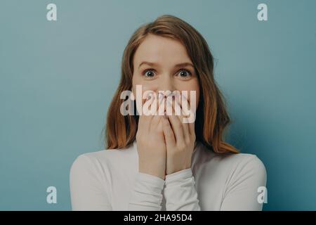 Charmant überrascht positive junge Frau schloss ihren Mund mit beiden Händen in Aufregung Stockfoto