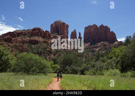 Zwei Wanderer auf dem Cathedral Rock Trail in der Nähe von Sedona, Arizona. Cathedral Rock in der Ferne ist eine natürliche Spitze oder aus rotem Sandstein. Stockfoto