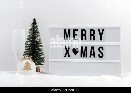 Weihnachtsbaum, Sektglas und Leuchtkasten mit Text FROHE WEIHNACHTEN auf einem Tisch. Minimales Weihnachts- oder Neujahrskonzept. Stockfoto