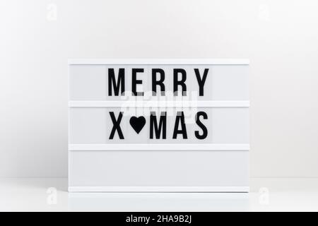 Leuchtkasten mit Text FROHE WEIHNACHTEN auf weißem Tisch. Minimales Weihnachts- oder Neujahrskonzept. Stockfoto