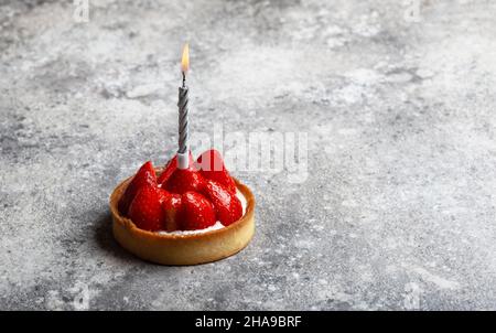 Erdbeerkuchen mit brennender Kerze auf grauem Hintergrund in Nahaufnahme Stockfoto