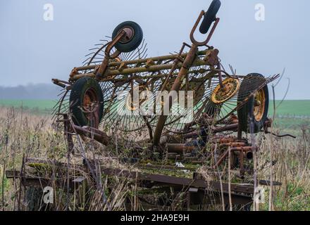Eine alte verlassene, rostende, überwuchert Landmaschinen Rake und Dreschmaschine Anbaugerät, Wiltshire UK Stockfoto