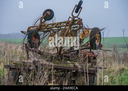 Eine alte verlassene, rostende, überwuchert Landmaschinen Rake und Dreschmaschine Anbaugerät, Wiltshire UK Stockfoto