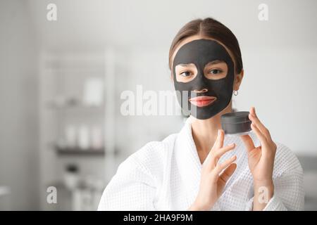 Junge Frau mit Aktivkohle-Maske auf ihrem Gesicht zu Hause Stockfoto