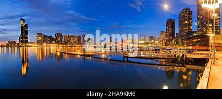 Breites Sonnenuntergangspanorama der Hafengegend von Melbourne und helle Beleuchtung der Straßenlaternen. Stockfoto