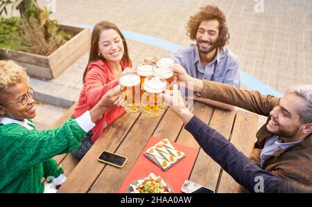 Fröhliche, multiethnische Freunde trinken Bier auf der Terrasse im Freien. Der Fokus liegt auf Bieren. Stockfoto