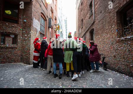 Blick von hinten auf die Nachtschwärmer, die sich während der Seattle SantaCon am Samstag, dem 11. Dezember 2021, auf der berühmten Gummimauer des Pike Place Market zu einem Gruppenfoto treffen. Die jährliche Kneipenbummel und Spendenaktion kehrte in diesem Jahr nach der Annullierung im Jahr 2020 aufgrund der Coronavirus-Pandemie zurück. Stockfoto