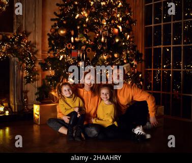Glückliche Familie Vater Mutter und zwei kleine Mädchen Töchter in gelben Pullover sitzen auf dem Boden zusammen während Weihnachten Stockfoto