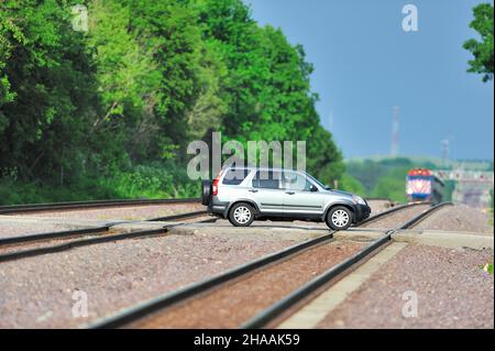 LAFOX, Illinois, USA. Ein Fahrzeug, das über Union Pacific fährt, fährt, während ein Metra-Pendlerzug auf der Landüberquerung abfährt. Stockfoto