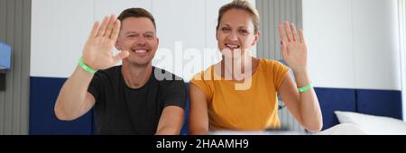 Mann und Frau sitzen im Hotelbett und winken mit der Hand zur Handykamera Stockfoto