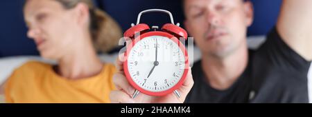 Schlafender Mann und Frau liegen im Bett und halten den roten Wecker in der Nähe Stockfoto