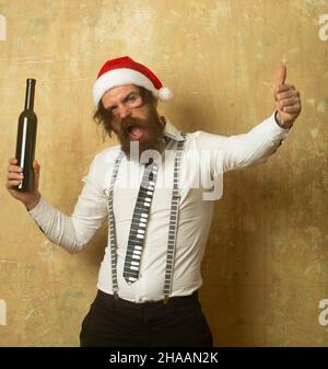 Schlecht betrunkener weihnachtsmann. Lustig aufgeregt Weihnachtsmann Alkohol in der Flasche über an der Wand Hintergrund trinken. Stockfoto
