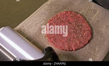 Kochen macht Fleisch Medaillons für Burger. Koch in schwarz Handschuhe macht Schnitzel essen. Die koteletts sind in Stahl Ring in eine noch Medaillon eingeebnet. Stockfoto