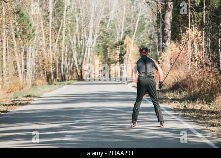 Training ein Athlet auf der Walze Skater. Biathlon Fahrt auf dem Roller Ski mit Skistöcke, im Helm. Herbst Training. Roller Sport. Stockfoto