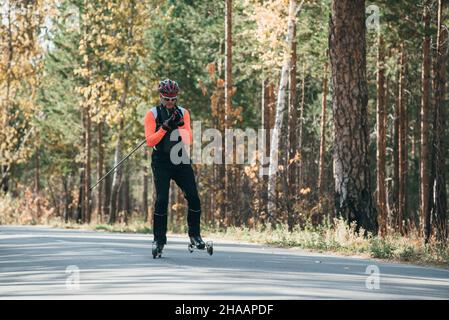 Training ein Athlet auf der Walze Skater. Biathlon Fahrt auf dem Roller Ski mit Skistöcke, im Helm. Herbst Training. Roller Sport. Stockfoto