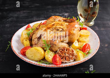 Gebackenes Huhn mit Kartoffeln auf einem weißen Teller. Dunkler Hintergrund. Stockfoto