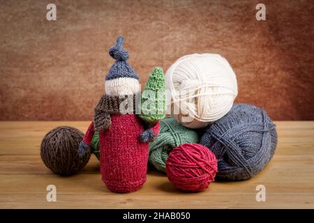 Handgefertigter gestrickter Gnome mit Weihnachtsbaum und Garnbällen auf einem Holztisch. Weihnachtskonzept. Stockfoto