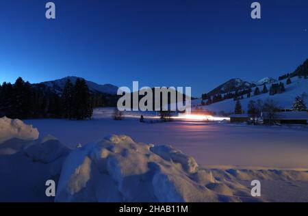 Bad Hindelang, Deutschland. 12th Dez 2021. Kurz vor Sonnenaufgang fährt ein Langlauffahrzeug auf der Loipe im Stadtteil Unterjoch. Quelle: Karl-Josef Hildenbrand/dpa/Alamy Live News Stockfoto