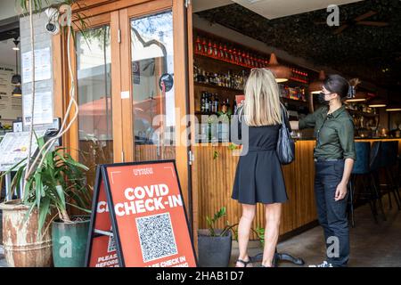 Einchecken mit QR-Code für Covid in einem Sydney Restaurant in Manly Lady Checks in assistiert von Kellnerin in schwarzem Facemark, covid 2021. Dezember, Sydney Stockfoto